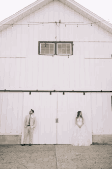 a bride and groom pose for a picture in front of a white barn