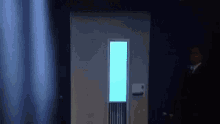 a man in a suit and tie is standing in front of a door with a blue light on it