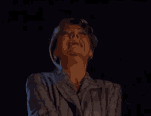 a woman in a suit and pearls is making a funny face in the dark .