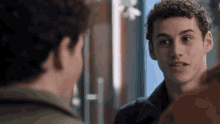 a young man with curly hair is talking to another man in a room .