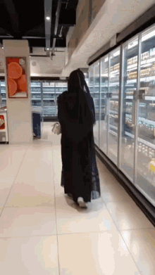 a woman in a black dress walks through a grocery store aisle