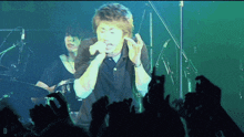 a man singing into a microphone with a crowd behind him