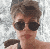 a young man wearing sunglasses and a tank top looks at the camera