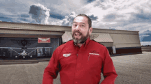 a man in a red shirt stands in front of a hangar with a plane in it
