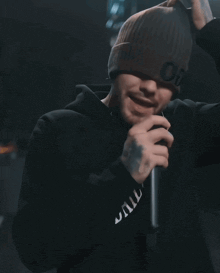 a man wearing a beanie with the letter o on it holds a microphone