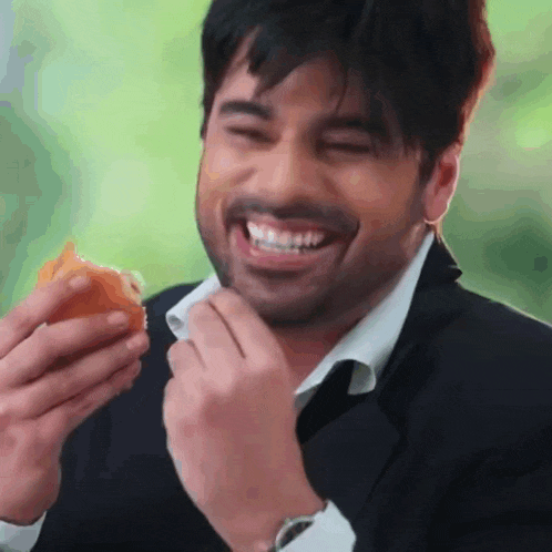a man in a suit is smiling while eating a hamburger