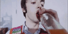 a man is drinking from a glass while wearing a sweater vest