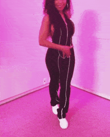 a woman in a black jumpsuit is standing in front of a purple wall