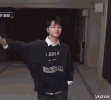 a young man in a black sweater is standing in a hallway with his arms in the air .