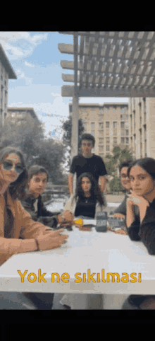a group of people sitting around a table with a sign that says yok ne sikils