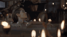 a woman is laying in a bathtub with candles surrounding her