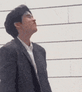 a man in a suit and white shirt is standing in front of a white wall and making a funny face .