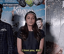 a woman is standing in front of a movie poster and says `` i love you , kat '' .