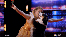 a woman in a gold dress is dancing with a black and white dog on a stage sponsored by nbc