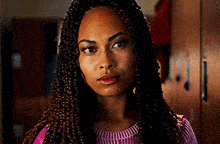a woman with braids is wearing a pink sweater and standing in a locker room .