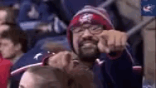 a man with a beard and glasses is sitting in a stadium holding a stick in his hand .