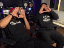 two men are making a heart shape with their hands and one has a shirt that says capitol