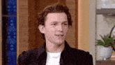 a young man wearing a black jacket and a white t-shirt is talking on a microphone .