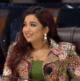a woman wearing a floral jacket and earrings is smiling