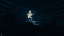 a man playing a guitar on a stage with the letter d in the corner
