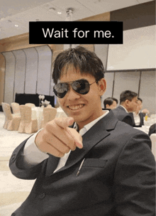 a man in a suit and sunglasses points at the camera with the words wait for me behind him
