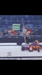 a wrestler is laying on the ground in a wrestling ring while a referee looks on
