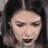 a close up of a woman 's face with dark lipstick and ear buds .