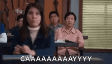 a group of people are sitting at desks in a classroom with a woman standing in front of them .