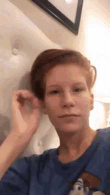 a young man with red hair is holding his ear while wearing a blue shirt with a toy story character on it .