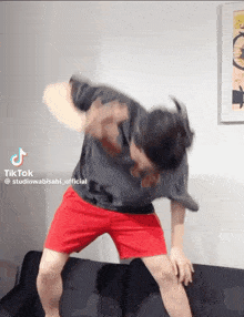 a man in a black shirt and red shorts is dancing on a couch with a tiktok watermark on the bottom