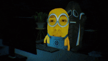 a yellow minion wearing overalls and goggles is sitting in front of a computer monitor