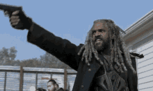a man with dreadlocks is holding a gun in his hand and pointing it at the camera .