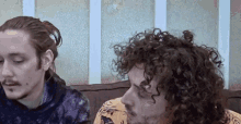 two men with curly hair are sitting next to each other on a couch looking at something .