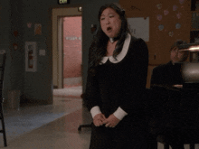 a woman in a black dress singing in front of a piano