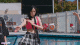 a girl in a plaid skirt is standing in front of a pool with a sign that says dogs