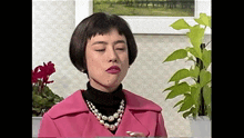 a woman wearing a pink coat and a pearl necklace