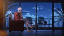 a man sits in a chair with his legs crossed in front of a large window