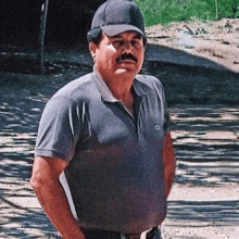 a man with a mustache wearing a hat and a lacoste shirt is standing with his hands in his pockets .