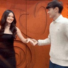 a man and a woman are holding hands in front of a wooden wall with a heart on it