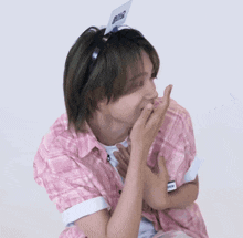 a man in a pink shirt is covering his mouth with his hands while sitting on a chair .