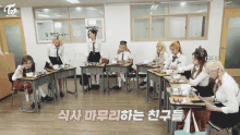 a group of girls sit at desks in a classroom with a twice logo on the wall