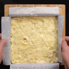 a person is holding a pan of food with a piece of wax paper covering it