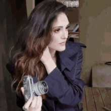 a woman in a trench coat holds a camera in her hand