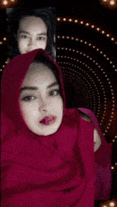 a woman wearing a pink hijab shows her tongue out