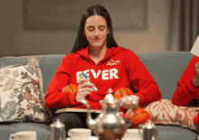 a woman is sitting on a couch wearing a red sweatshirt that says ever