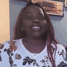 a woman wearing a floral shirt is smiling in front of a picture of a savannah