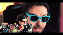 a man wearing blue sunglasses and a black hat is holding a remote control