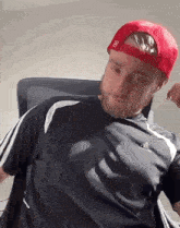 a man with a beard wearing a red hat and a gray shirt is sitting in a chair .