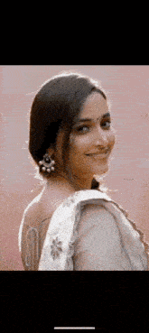 a woman wearing a white saree and earrings is smiling and looking over her shoulder .
