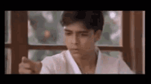 a young man in a white karate uniform is sitting in front of a window .